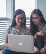 two smiling women starring on silver MacBook inside well-lit room