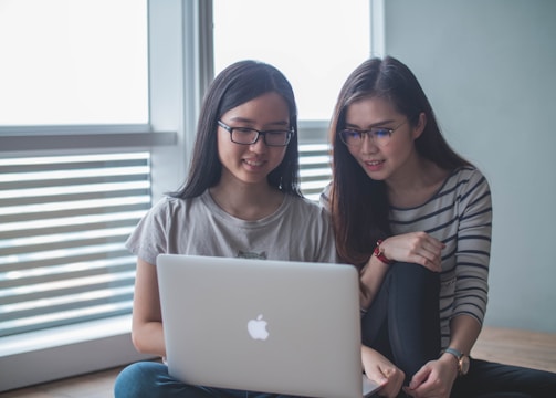 two smiling women starring on silver MacBook inside well-lit room
