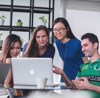 four people watching on white MacBook on top of glass-top table